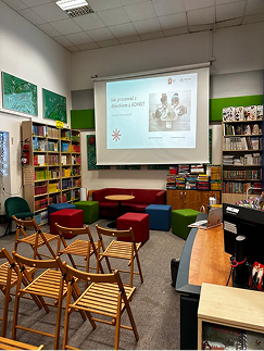 Sala w bibliotece przygotowana na spotkanie: rzędy krzeseł i ekran z prezentacją